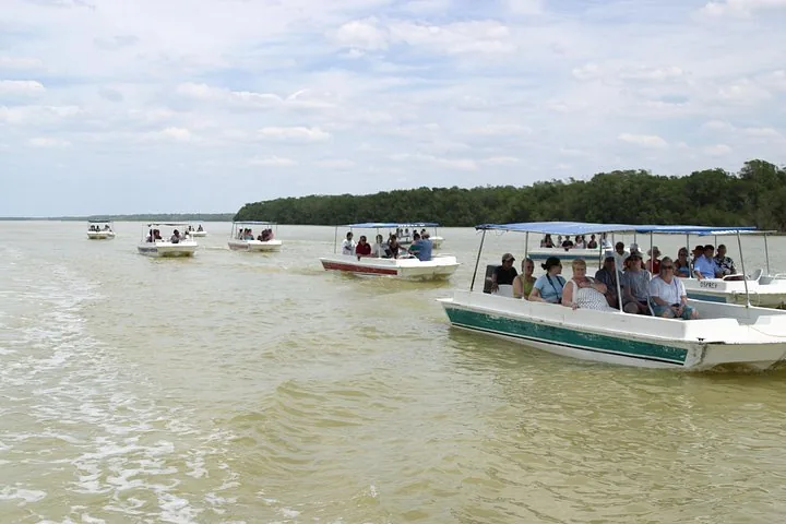 Several small boats filled with tourists travel across a wide body of water.